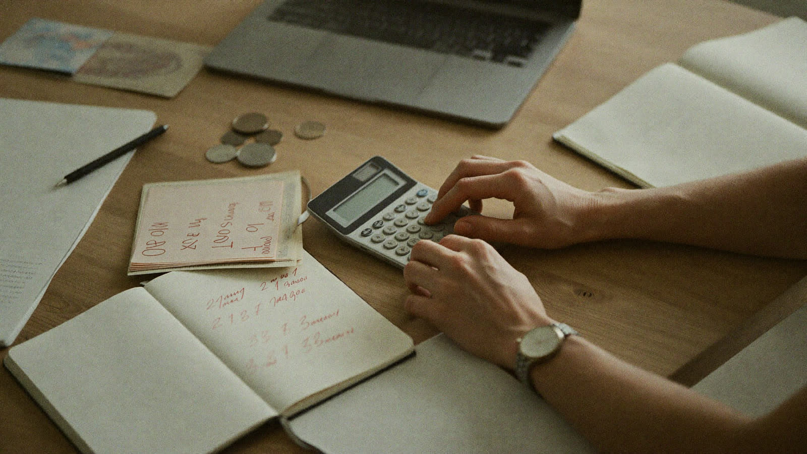 Manos de un emprendedor haciendo cuentas con calculadora, cuaderno y laptop