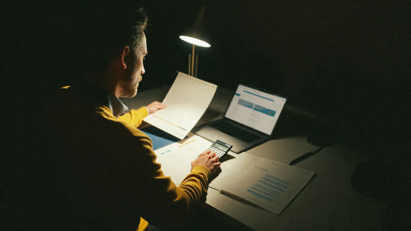 Empresario revisando cifras con calculadora y gráficas junto a su laptop